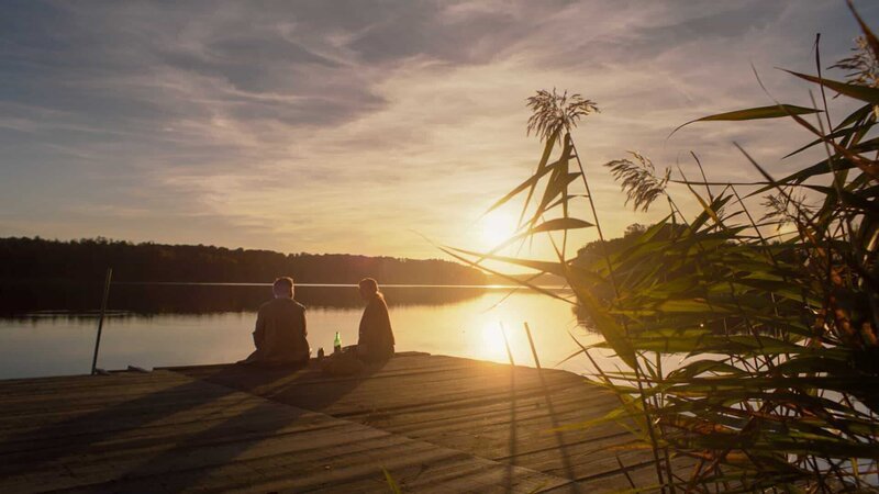 Ballouz (Merab Ninidze) und Eva (Helene Grass) picknicken auf einem Steg an einem See bei Sonnenuntergang. – Bild: ZDF und X Filme /​ Ben F. Wieg.