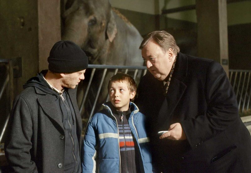 Gregor Ehrenberg (Dieter Pfaff, r.) trifft Ortwin Posche (Rainer Strecker, l.) und dessen Sohn Andreas (Willi Gerk, l.) heimlich im Elefantenhaus im Zoo. – Bild: HR/​ARD/​Marion von der Mehden
