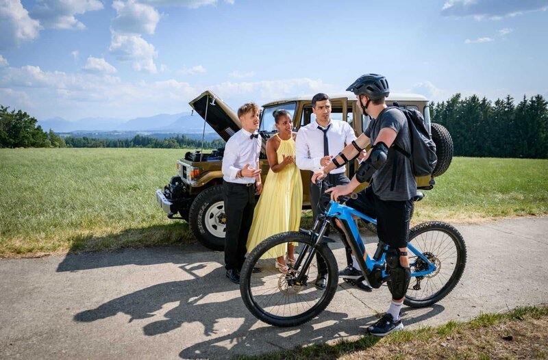 Leander (Marcel Zuschlag, 2.v.r. mit Stefan Hartmann, l. & Belina Mohamed-Ali, 2.v.l.) leiht sich ein Fahrrad, um es noch rechtzeitig zur Trauung zu schaffen. – Bild: ARD/​WDR/​Christof Arnold