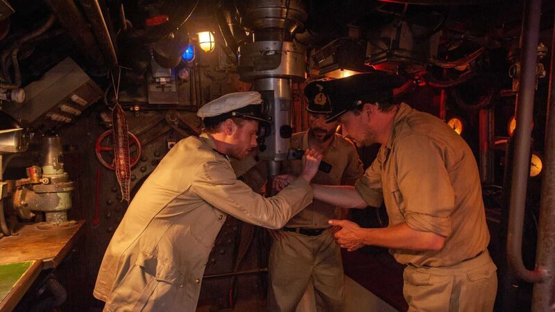Symbolbild: Ein U-Boot-Kommandant blickt durch das Sehrohr eines U-Bootes und sichtet ein Schiff. Um das Sehrohr herum stehen zwei Offiziere. – Bild: ZDF und Harald J.Braun./​Harald J.Braun