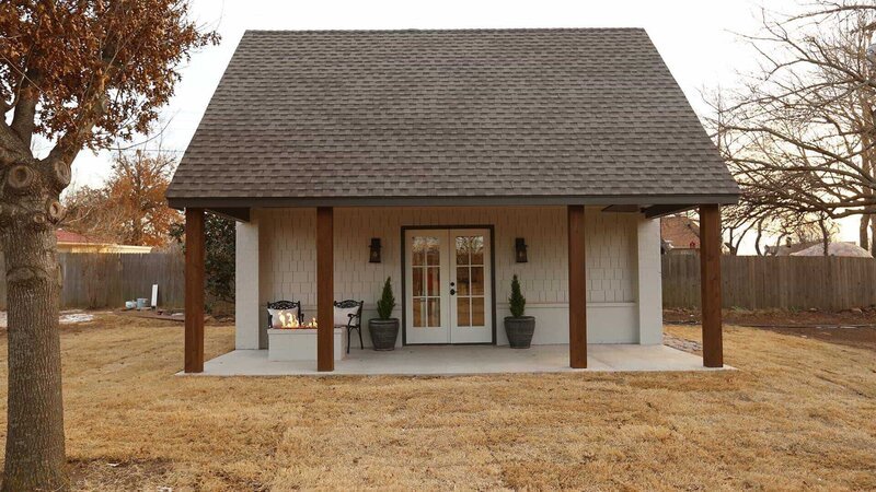Asymmetrically stylish, the fire pit on the front porch adds interest and begs for attention, whereas the symmetry of the build itself, offers a stately simplicity. The front pillars compliment the leaves on the dormant tree and the roof compliments the picket fence behind, all of which, contrasts the painted brick and faux shake shingle siding, in El Reno, Oklahoma, as seen on Tiny House, Big Living. – Bild: 2018, Scripps Networks, LLC. All Rights Reserved.