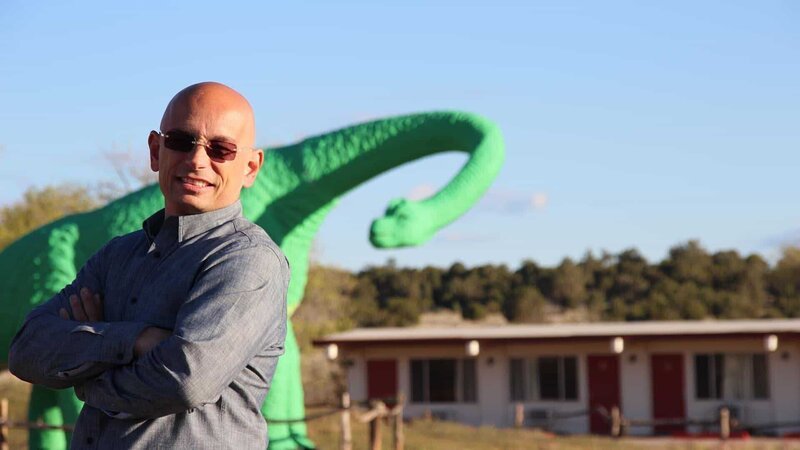 Host Anthony Melchiorri poses in front of a dinosaur statue outside the Grand Canyon Caverns on Historic Route 66, as seen on Travel Channel’s Hotel Impossible. – Bild: 2015, The Travel Channel, L.L.C. All Rights Reserved.