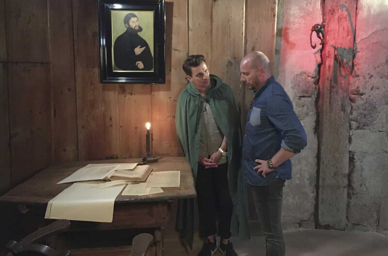 Martin Luther und der Teufel: Julian Sengelmann lässt sich von Nino Dell die Geschichte des Tintenklecks erklären. – Bild: MDR/​EIKON Nord