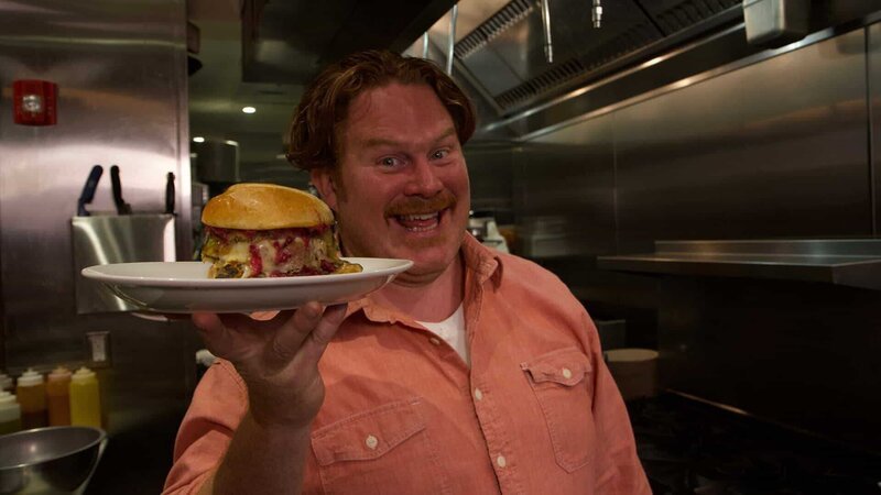 Man v. Food’s Casey Webb posing with The Pilgrim Burger, a Thanksgiving-themed turkey burger, as seen on the Travel Channel. – Bild: 2017,The Travel Channel, L.L.C. All Rights Reserved