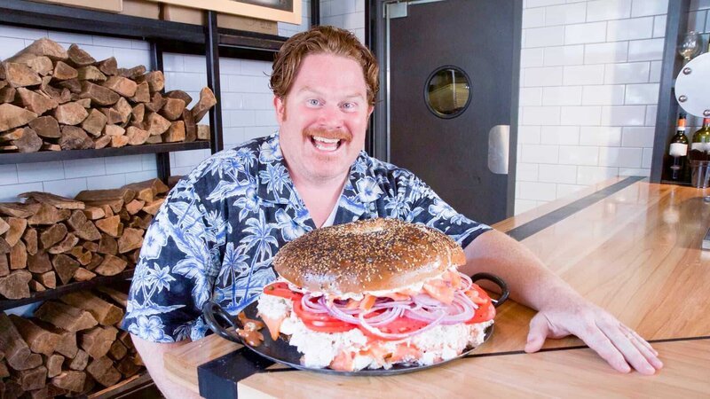 Host Casey Webb poses with Spread Bagelry’s 13-pound Classic Whale Challenge, as seen on Travel Channel’s Man v. Food. – Bild: 2017,The Travel Channel, L.L.C. All Rights Reserved