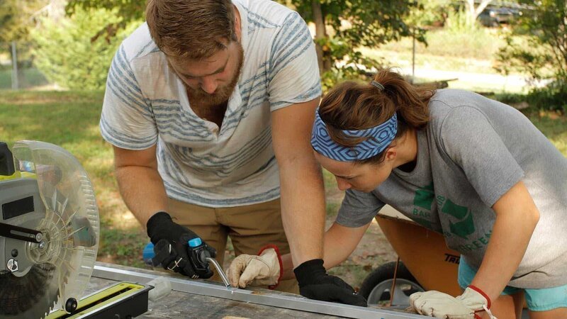 Kathrin and Tyler apply a piece of solder with a small torch to connect two pieces of aluminum, square stock that will be used to create the track system for the sliding, stowaway deck on the end of their tiny home, in Rossville, Georgia, as seen on Tiny House, Big Living. – Bild: 2018, Scripps Networks, LLC. All Rights Reserved.