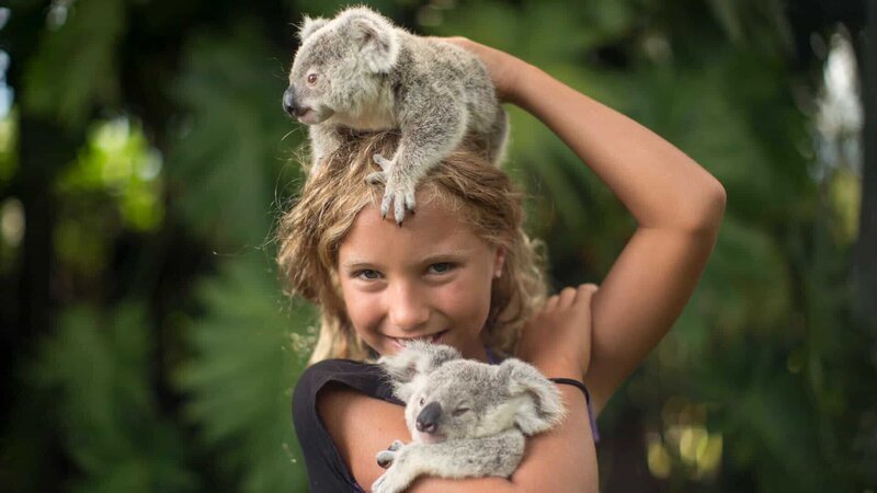 Izzie holding two koalas smiling at the camera. – Bild: Discovery Communications