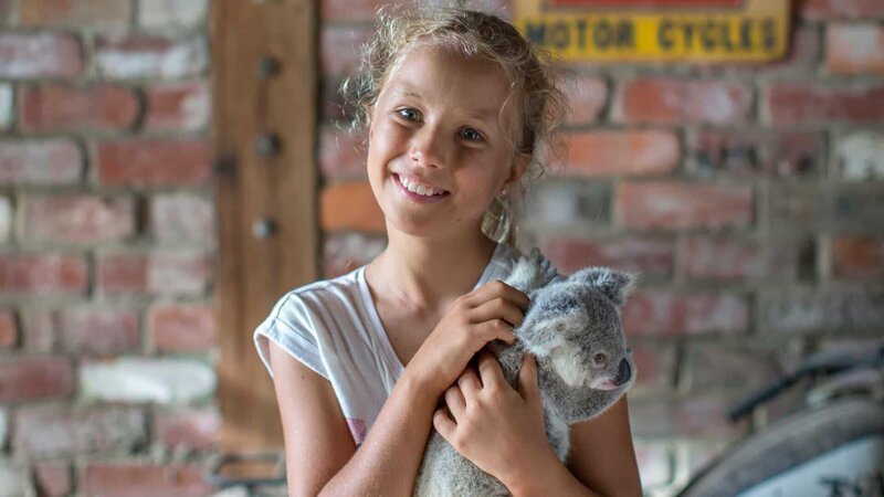 Izzie smiling at the camera holding koala. – Bild: Discovery Communications