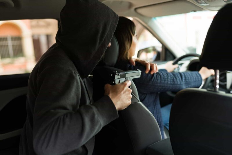 Rückansicht eines Verbrechers, der eine junge Frau mit einer Waffe bedroht, um ihr Auto zu stehlen. – Bild: Shutterstock /​ Shutterstock /​ Copyright (c) 2022 antoniodiaz/​Shutterstock. No use without permission.