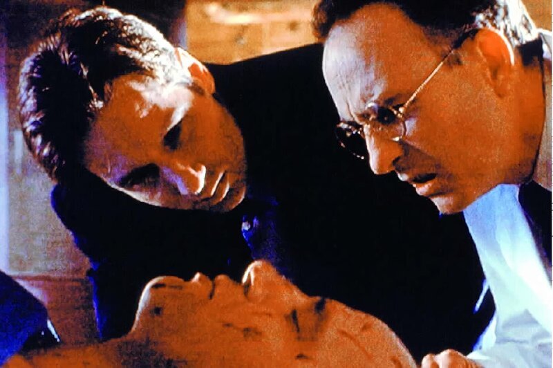 Mulder (David Duchovny, l.) und der Gerichtsmediziner (Laurie Murdoch, r.) finden einen merkwürdigen Holzsplitter im Hals des toten Mr. Balocchi (Gardiner Millar, M.). – Bild: SYFY