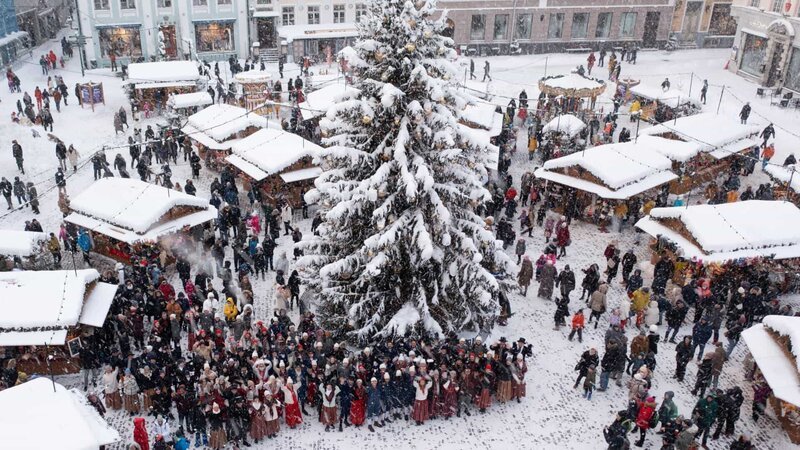 Eine Gruppe estnischer Volkstänzer steht um den Weihnachtsbaum auf dem Talliner Weihnachtsmarkt. (National Geographic) – Bild: National Geographic /​ National Geographic