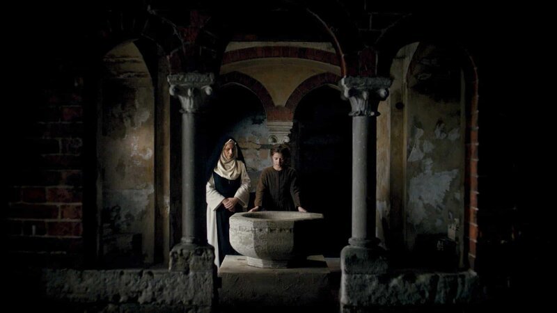 L-r: Äbtissin (Daniela Holtz) und Anna Magaretha, Kind (Paula Pastare) vor einem Taufbecken im Kloster von Egeln stehend. – Bild: LOOKSfilm