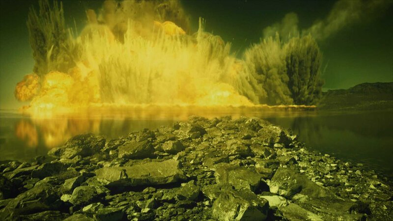 Felsen aus der Nähe, Explosion in der Ferne. – Bild: Warner Bros. Discovery