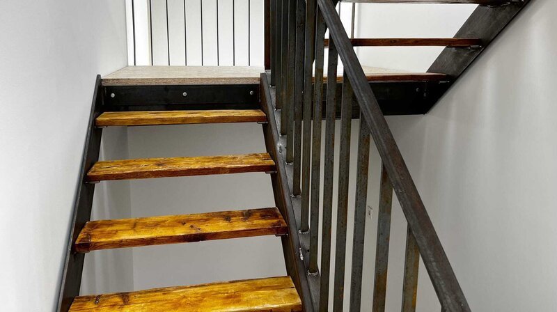 Die Stahltreppe mit Stufen aus alten Gerüstbohlen führt von Erdgeschoss über das Obergeschoss bis ins Dachgeschoss. – Bild: NDR/​Rainer Mueller-Delin /​ NDR Presse und Information