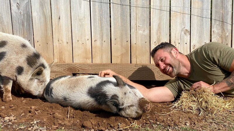 Lee Asher mit zwei Schweinen vor einem Holzzaun. – Bild: Dan Jesperson /​ Group Nine Media, Inc. /​ Photobank. /​ Discovery Communications, LLC