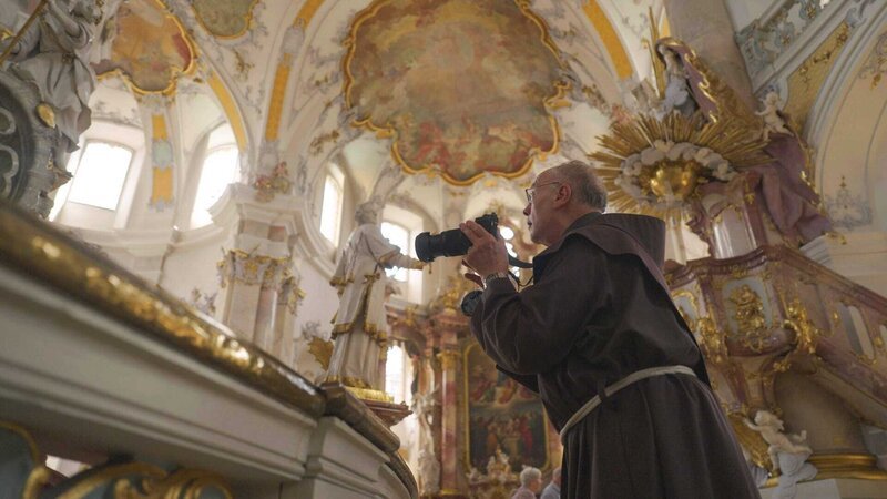 Im Bild: Pater Werner Reischmann beim fotografieren der Heiligenstatuen in der Basilika von Vierzehnheiligen. – Bild: ORF /​ Metafilm/​Tellux Film