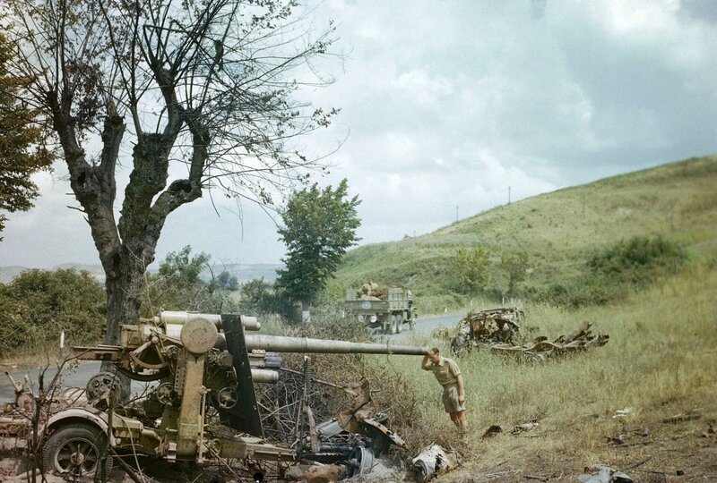 „Ein zerstörter deutscher Transport markiert den Rückzug aus Rom, 18. Juni 1944 Ein britischer Soldat untersucht ein zerstörtes deutsches 88-mm-Geschütz nördlich von Rom. Im Hintergrund fährt ein amerikanischer Lastwagen vorbei. – Bild: THE HISTORY CHANNEL /​ © WildBear Entertainment 2023