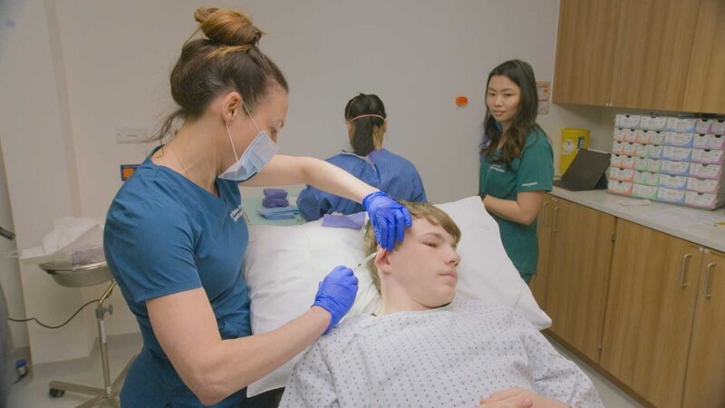 Mid shot of Dr Emma injecting Harley’s ear Keloid before surgery. Nurse Mottie and Nurse Rosie in background.. – Bild: 2021, Discovery, Inc. All Rights Reserved.