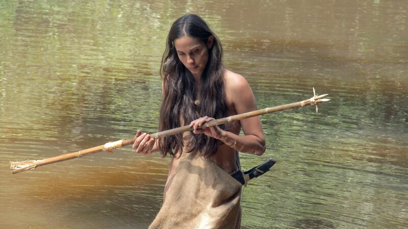 Ax Porath standing in the shallow water of a river examining a spear in Guyana. – Bild: Discovery Channel /​ Photobank 33885_ep204_039 /​ Discovery Communications