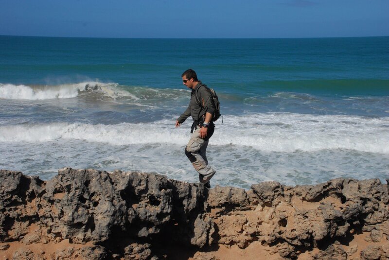 Bear Grylls walking over rocks with waves breaking in the background. – Bild: Copyright: Discovery Communications, Inc. For Show Promotion Only