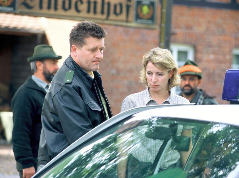 Dorfpolizist Schulz (Bruno F. Apitz) geleitet die verstörte Birgit Sofsky (Kirsten Block), die gerade ihren Mann beim Jagdunfall verloren hat, nach Hause. – Bild: MDR/​Hardy Spitz