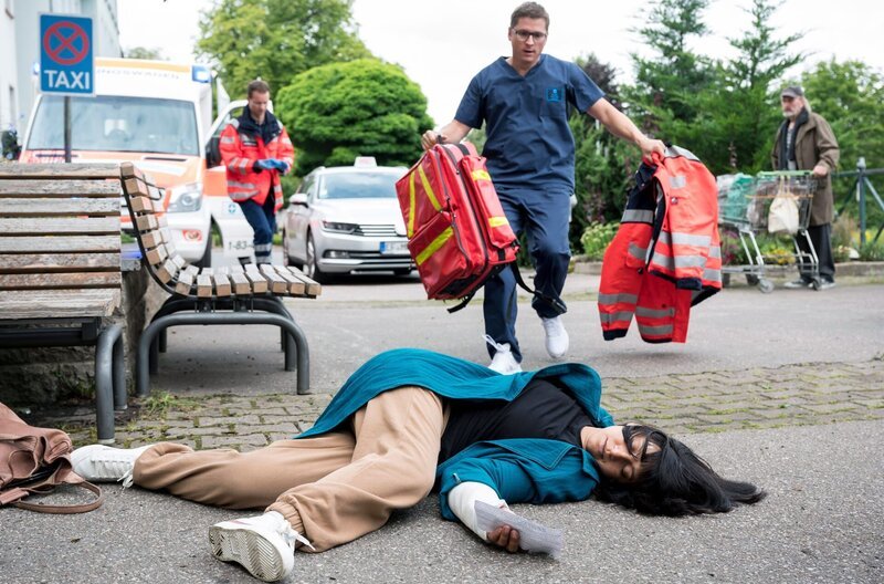 Dr. Elias Bähr (Stefan Ruppe, h.M. mit Komparsen) eilt seiner Ex-Frau Ameena Schneider (Mira Mazumdar, v.) zur Hilfe. – Bild: ARD/​Jens-Ulrich Koch