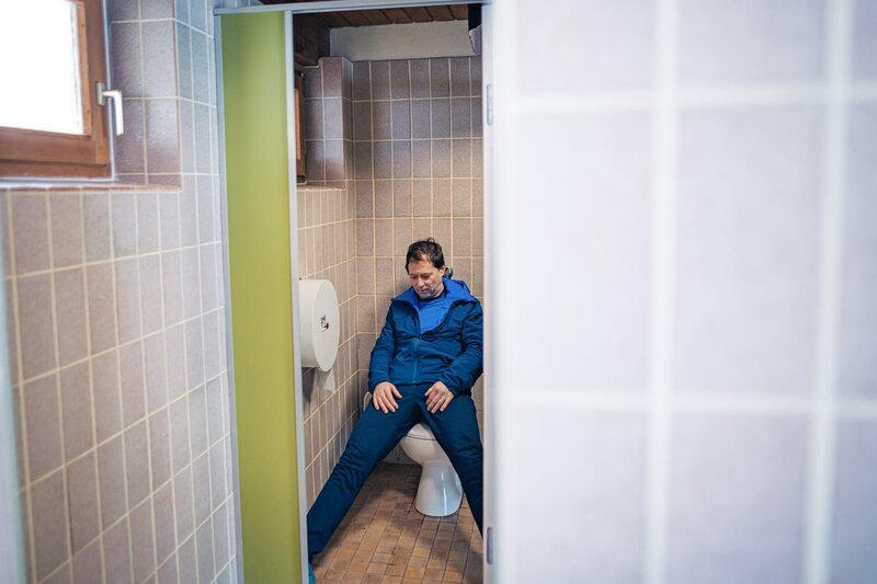 Ein Toter (Komparse) liegt in einer der Toilettenkabinen. – Bild: 2022 LEONINE Studios /​ Jenrick Mielke