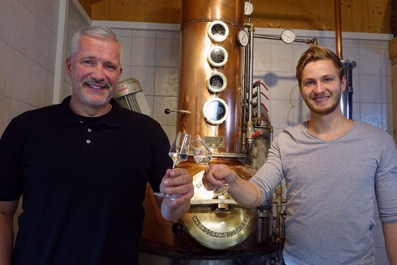 Kajetan Schnitzer (links) und Alexander Herrmann posieren mit einem Glas Heugeist, Destillerie Schnitzer in Kaltenbach (Landkreis Traunstein). – Bild: Jürgen Endriß /​ BR /​ BR/​Jürgen Endriß