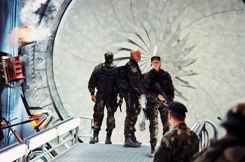 Sam (Amanda Tapping, r.), Daniel (Michael Shanks, l.) und Teal’c (Christopher Judge, M.) können sich nach einem Jaffa-Angriff auf die Erde retten und erstatten Bericht. O’Neill bleibt auf dem Planeten mit einem Leutnant zurück, an den sich in der Stargate Zentrale keiner erinnert … – Bild: AXN Sci-fi