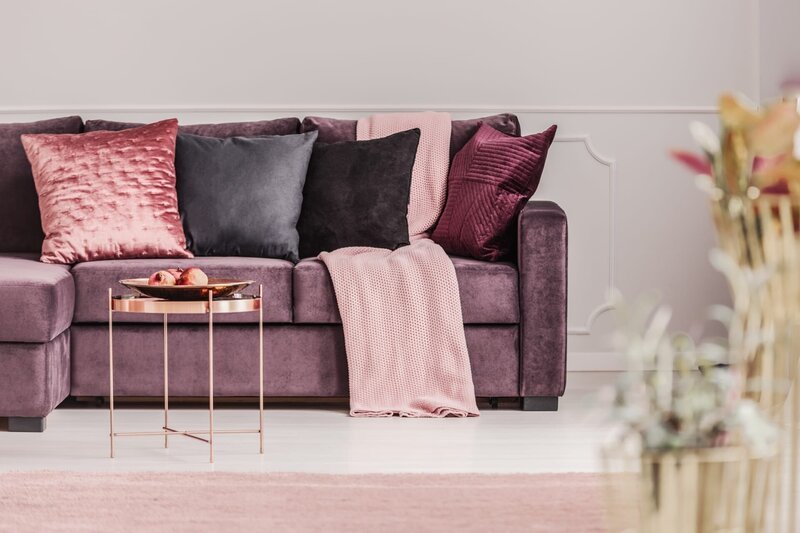 Kupfertisch vor einer violetten Couch mit dekorativen Kissen im eleganten Wohnzimmerinterieur – Bild: Deposithotos /​ Photographee.eu /​ Katarzyna Bialasiewicz