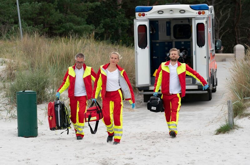 Nora Kaminski (Tanja Wedhorn) und ihr Kollege Lars Hinrichs (Bo Hansen) sowie ein weiterer Sanitäter (Wolfgang Stadler) eilen zu einem Notfall am Strand. – Bild: ARD Degeto/​Boris Laewen