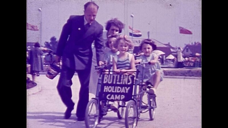 Mann, Frau und drei Kindern,die einen Wagen schieben auf dem steht „BUTLINS HOLIDAY CAMP“ – Bild: RTL /​ © Azor Producciones /​ East Anglian Film Archive