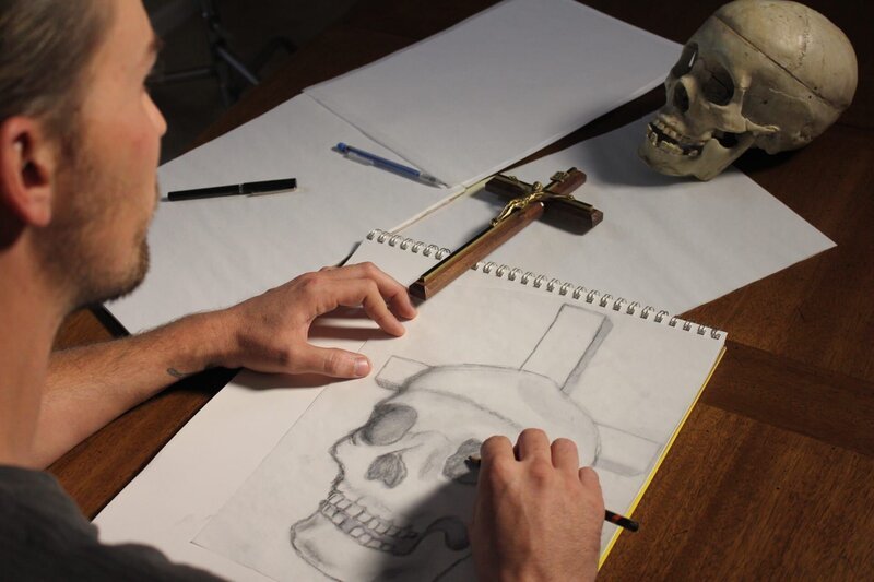 Nick sketching drawings of a skull at the table. – Bild: Destination America /​ Discovery Communications