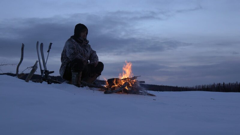 Alex Javor sitzt bei eisigen Temperaturen an einem warmen Feuer. (National Geographic) – Bild: National Geographic /​ National Geographic