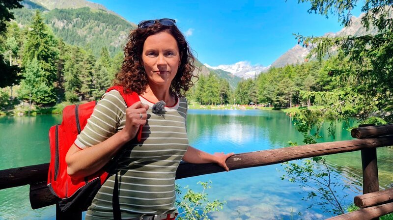 Moderatorin Anne Wilmes vor dem Lexert in Bionaz, der zu den vielen glasklaren Bergseen des Aostatals gehört. – Bild: WDR/​Alice Tschöke