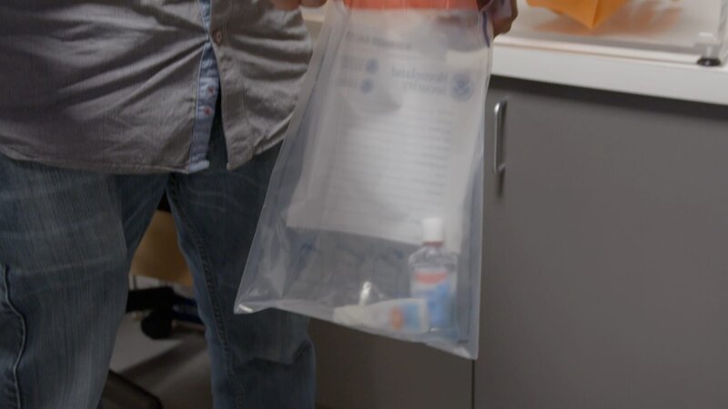 CBP-Beamter Rivera hält einen Beutel mit Beweismaterial offen, in den die mit Ketamin gefüllten Flaschen, die im Gepäck eines Verdächtigen gefunden wurden, geworfen werden.(National Geographic) – Bild: National Geographic /​ National Geographic