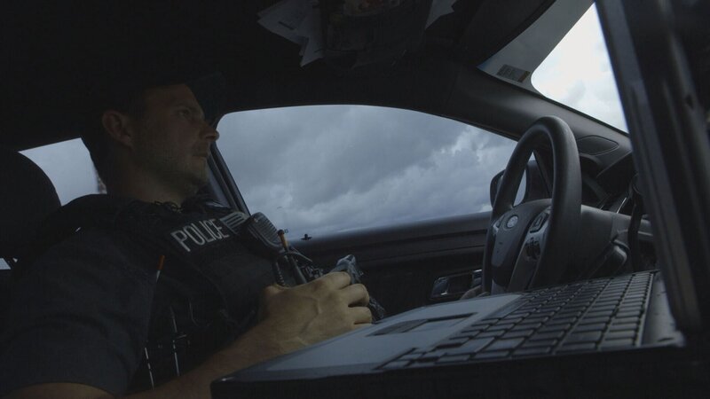 Polizist sitzt in einem Auto – Bild: Crime + Investigation /​ A+E Networks