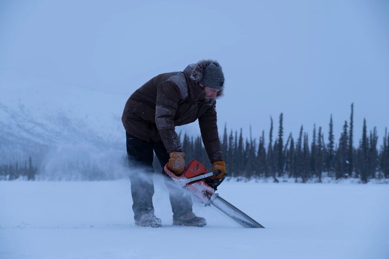 Johnny Rolfe sägt mit der Kettensäge Löcher ins Eis, um ein Fischernetz unter dem zugefrorenen See auszulegen (National Geographic/​Mike Fennell). – Bild: National Geographic /​ Mike Fennell /​ National Geographic/​Mike Fennell