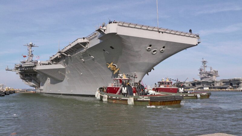 Zwei Spezialschlepper helfen dem 95 tausend Tonnen schweren Flugzeugträger vor Beginn des Manövers aus dem Hafen hinaus auf offene See zu steuern. – Bild: N24 Doku