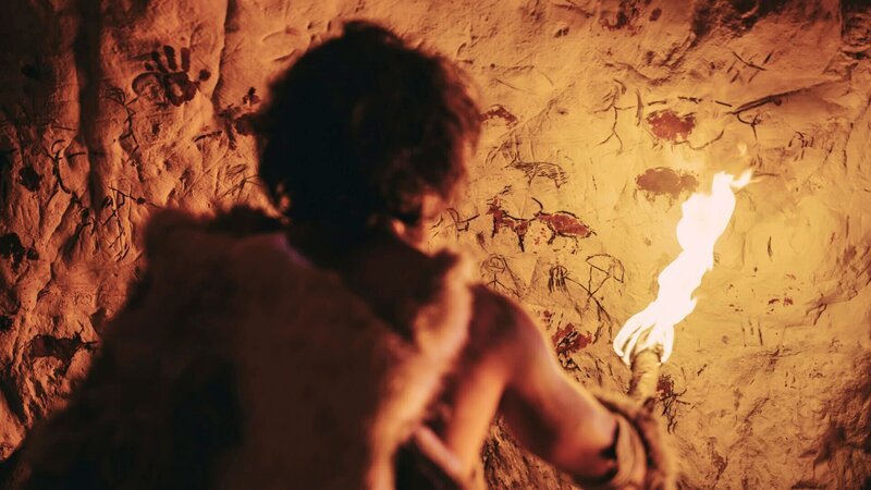 The Riddle of the Carpathian Sphinx, Die Sphinx der Karpaten Primeval Caveman Wearing Animal Skin Standing in His Cave At Night, Holding Torch with Fire Looking at Drawings on the Walls at Night. Cave Art with Petroglyphs, Rock Paintings. Back View – Bild: otf /​ OANAGHIOCEL@2010< /​ The History Channle