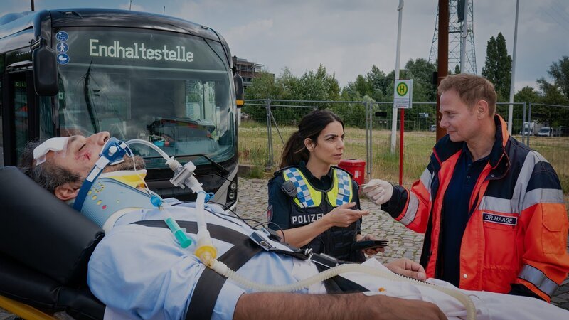 Dr. Haase (Fabian Harloff, r.) übergibt Isa (Lilli Hollunder) den Ausweis des verletzten Busfahrers (Majid Bakhtiari, l.). – Bild: ZDF und Boris Laewen (bola).