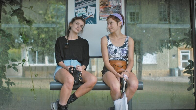 Von links: Zoë (Violet Braeckman, l.) und Ylena (Laurian Callebaut, r.) sitzen auf der Bank einer Bushaltestelle. Werden sie ihre Freundin Lisa wiederfinden? – Bild: ZDF und Sofie Gheysens./​Sofie Gheysens