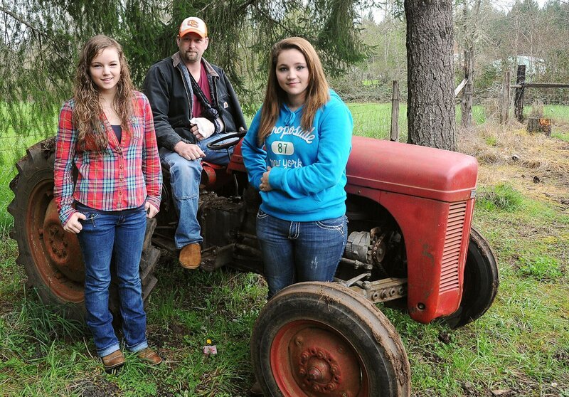 Jeff Smith sitzt am Samstagnachmittag rittlings auf seinem Traktor neben seinen Töchtern Hannah, 16, und Haylee, 14, in seinem Haus im McDowell Creek Park. (Jesse Skoubo/​Mid-Valley Sunday) – Bild: CORVALLIS_Gazette_Times