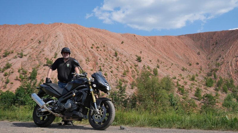 Bernd Schmelzer mit seinem MZ-Motorrad vor der Abraumhalde des ehemaligen Bischofferöder Kaliwerks „Thomas Müntzer“. 1993 hatte der ehemalige Kumpel 15 Tage für den Erhalt des Kaliwerks gehungert. Nach der Schließung war der 62-jährige arbeitslos und hat später zum CNC-Dreher umgeschult. Heute engagiert er sich im Kalimuseum von Bischofferode. – Bild: MDR/Malte Niessen Bernd Schmelzer mit seinem MZ-Motorrad vor der Abraumhalde des ehemaligen Bischofferöder Kaliwerks „Thomas Müntzer“. 1993 hatte der ehemalige Kumpel 15 Tage für den Erhalt des Kaliwerks gehungert. Nach der Schließung war der 62-jährige arbeitslos und hat später zum CNC-Dreher umgeschult. Heute engagiert er sich im Kalimuseum von Bischofferode. – Bild: MDR/Malte Niessen