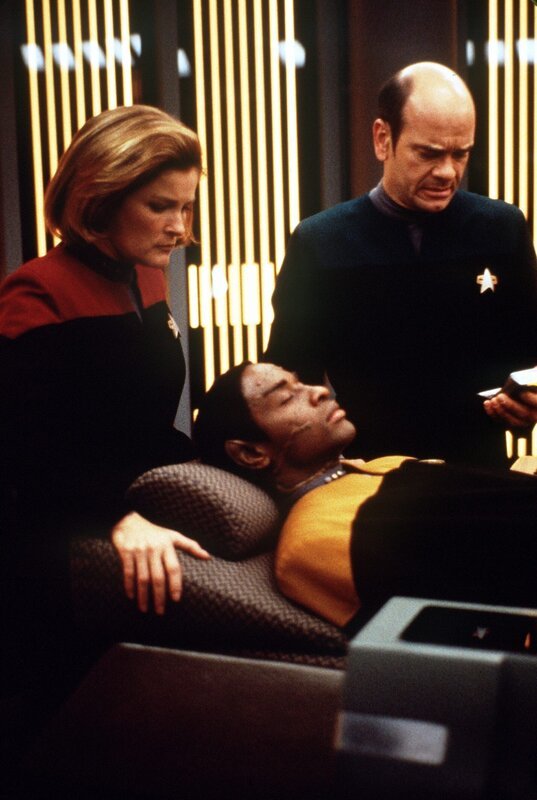 Der Doktor (Robert Picardo, r.) und Captain Janeway (Kate Mulgrew, l.) sind besorgt um Tuvok (Tim Russ, liegend), der nach einem Angriff fremder Wesen ins Koma gefallen ist. – Bild: Tele 5