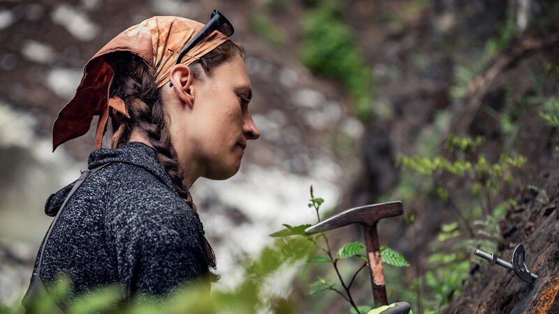 Kayla Johanson hält einen Hammer, um Schrauben in einer Bergwand zu befestigen. – Bild: Warner Bros. Discovery