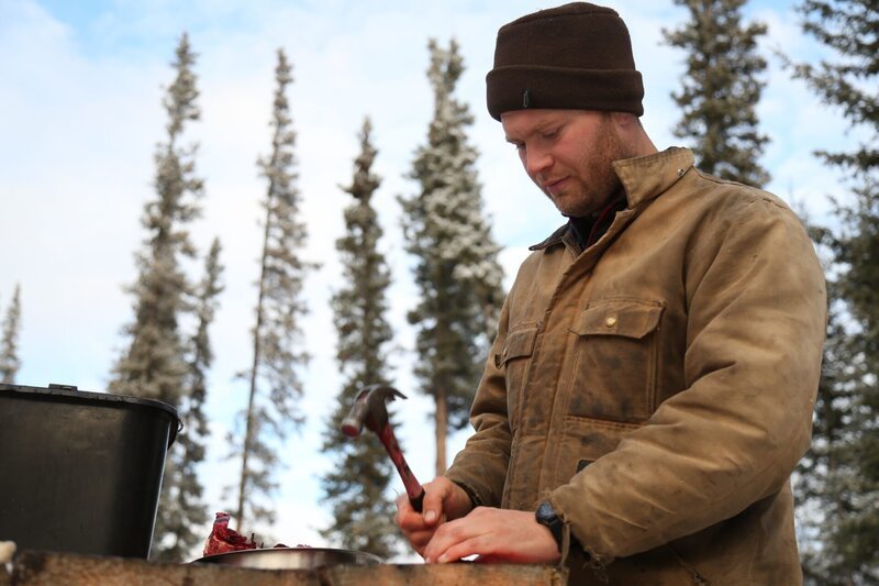 Tyler cutting meat at a table outside. – Bild: Animal Planet /​ Discovery Communications
