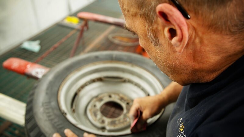 Ein Mechaniker arbeitet an Reifen. – Bild: Warner Bros. Discovery