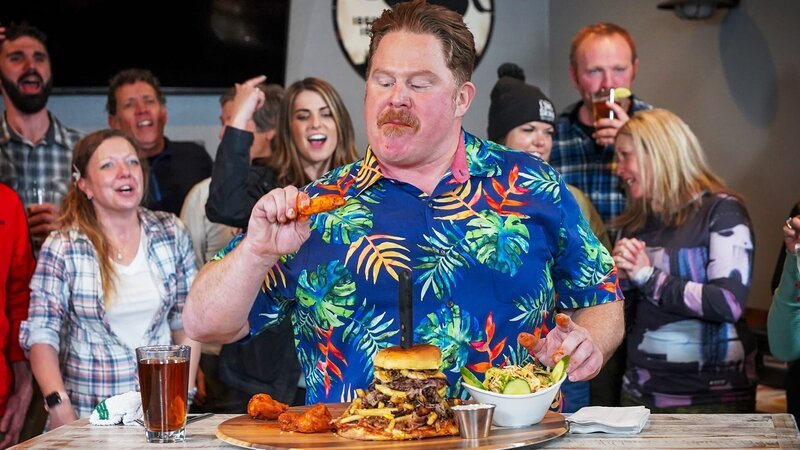 Host Casey Webb taking on the Menu Burger Challenge at Fox and Hound in Lake Tahoe as seen on Man v. Food, season 6. – Bild: Warner Bros. Discovery