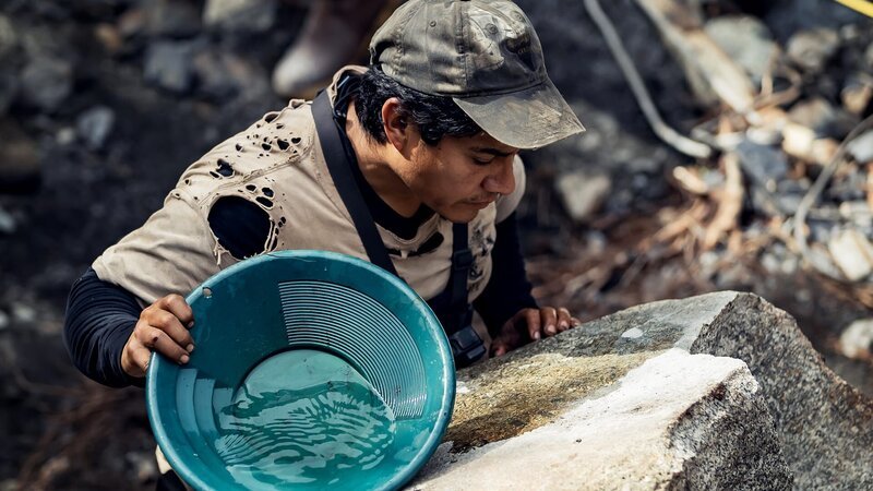 Carlos Minor hält eine Goldpfanne und betrachtet einen Felsbrocken – Bild: Warner Bros. Discovery